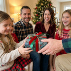 Family exchanging a gift in evergreen Christmas wrapping paper with red ribbon by Wrapped Studios.