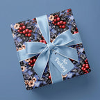 Elegant winter floral Christmas wrapping paper with blue bow and gift tag by Wrapped Studios.