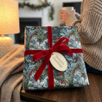 Luxury Christmas wrapping paper with botanical pine pattern and a red velvet bow by Wrapped Studios.
