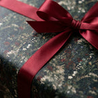 Dark floral wrapping paper with a burgundy satin bow. Elegant luxury gift wrap by Wrapped Studios.
