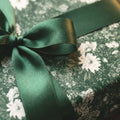 Elegant dark green floral wrapping paper with green satin bow, luxury gift wrap by Wrapped Studios.