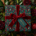 Luxury Christmas floral wrapping paper with red velvet bow and gift tag by Wrapped Studios.