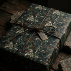 Dark vintage floral wrapping paper from Wrapped Studios tied with a leather bow on rustic wood.