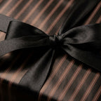 Close-up of a gift wrapped in striped brown wrapping paper with a black satin bow, for a modern, elegant gift.