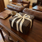 Elegant gift wrapped in striped paper with an ivory bow, sitting on a wooden table.