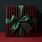 Elegant Christmas gift wrap with green satin bow and "Merry Christmas" tag on striped red and black wrapping paper.