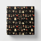Square gift wrapped in black Christmas wrapping paper with cats and decorated tree pattern tied with black ribbon.