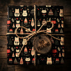 Square gift wrapped in black holiday wrapping paper with red and white cats and decorated trees, tied with twine and a wood tag.