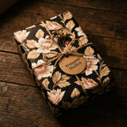 Dark vintage floral wrapping paper by Wrapped Studios on a gift box with a twine bow and rustic wood background.
