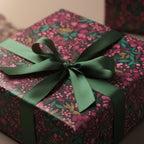 Close-up of a square gift wrapped in dark floral wrapping paper with a green satin ribbon and bow.