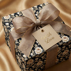 Elegant black floral wrapping paper with gold ribbon and 'With Love' tag by Wrapped Studios.