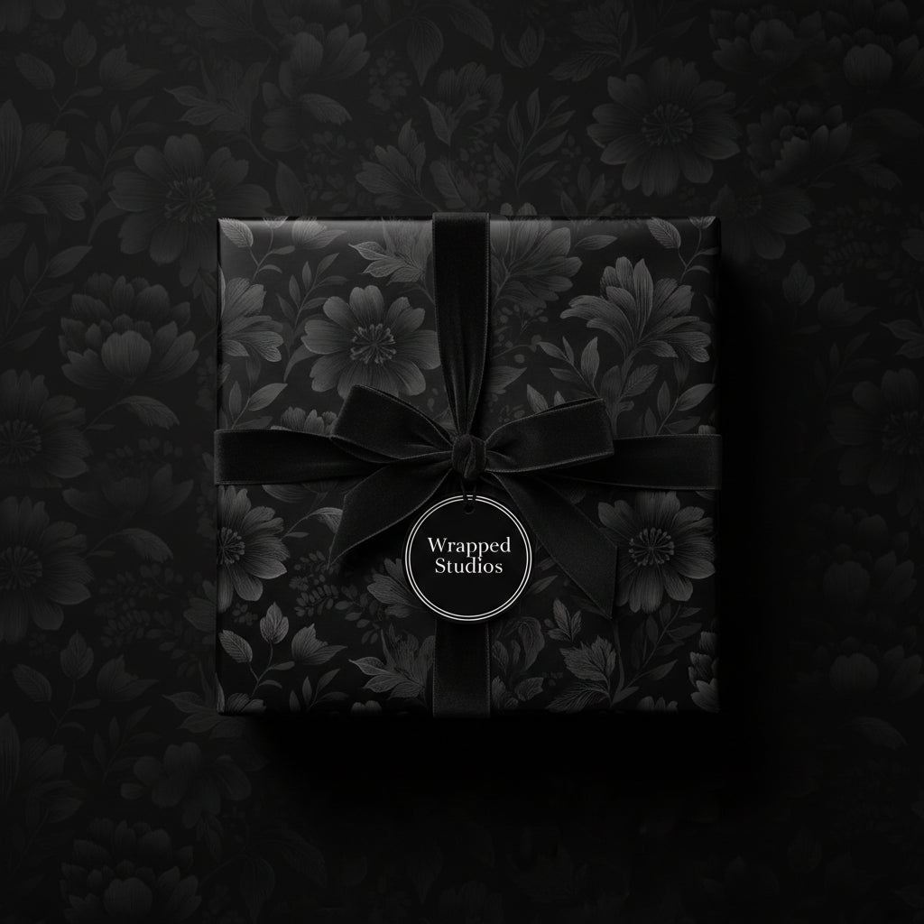 Elegant black floral wrapping paper on a square gift box tied with a velvet ribbon and tag.