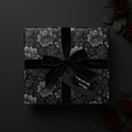 Elegant square gift box wrapped in black floral wrapping paper with velvet ribbon.
