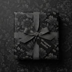 Elegant black floral wrapping paper with gray ribbon and "Wrapped Studios" tag for luxurious gift presentation.