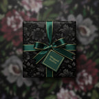 Elegant floral wrapping paper in black with a satin emerald ribbon and gold trim.