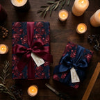 Luxury burgundy and navy floral wrapping paper with satin bows on a candlelit table by Wrapped Studios.