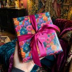 Luxury floral wrapping paper by Wrapped Studios on a gift box with a magenta ribbon and pink heart tag.