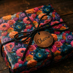 Vibrant dark floral wrapping paper by Wrapped Studios on a gift box with black twine and a Cheers tag.