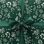 Close-up of a gift wrapped in elegant, dark green floral wrapping paper, tied with a matching green satin ribbon.