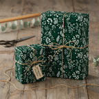 Elegant gifts wrapped in dark green floral wrapping paper with twine bows on a wooden table.