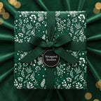 Elegant gift wrapped in dark green floral wrapping paper with matching ribbon and tag.