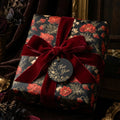 Luxury dark floral wrapping paper on a gift box with a red velvet bow by Wrapped Studios.