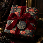 Luxury dark floral wrapping paper on a gift box with a red velvet bow by Wrapped Studios.