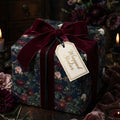 Moody floral wrapping paper by Wrapped Studios on a gift box tied with a luxury burgundy velvet ribbon.