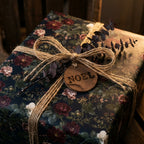Moody floral Christmas gift wrap by Wrapped Studios, featuring a rustic twine bow and wooden Noel tag.
