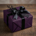 Elegant plum wrapping paper with black satin ribbon and bow, perfect for luxury gift giving.