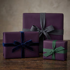 Elegant eggplant purple gift wrapping paper with velvet and grosgrain ribbon on wood table.
