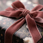 Moody floral wrapping paper with a dusty rose velvet ribbon bow on a gift by Wrapped Studios.