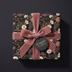 Luxury dark floral wrapping paper with a dusty pink velvet ribbon bow on a gift box by Wrapped Studios.