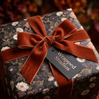 Moody floral wrapping paper by Wrapped Studios with a burnt orange velvet ribbon on a luxury gift box.
