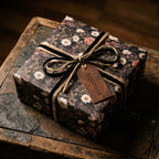 Dark vintage floral wrapping paper with black ribbon and leather tag on a rustic gift box by Wrapped Studios.