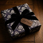 Luxury purple floral wrapping paper by Wrapped Studios on a gift box with a black velvet bow and "For Him" tag.