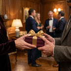 Luxury burgundy gift wrap with a gold bow being exchanged at an elegant holiday party by Wrapped Studios.