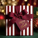 Red and white striped luxury Christmas gift wrap with a burgundy bow and tag by Wrapped Studios.