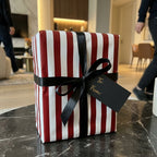 Red and white striped Christmas wrapping paper with black satin bow and tag by Wrapped Studios.