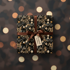 Elegant Christmas gift wrapped in black floral wrapping paper with brown ribbon and a gift tag.