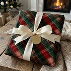 Plaid Christmas wrapping paper with a cream satin bow by Wrapped Studios in a cozy holiday fireplace setting.