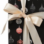 Elegant black Christmas wrapping paper with festive ornament pattern and a luxurious cream satin bow, perfect for holiday gifts.