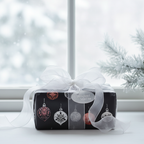 Elegant black Christmas wrapping paper with metallic ornament pattern and sheer white ribbon, perfect for holiday gifts.