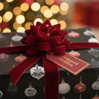 Black Christmas ornament wrapping paper with a plush red velvet bow and "Wrapped Studios" gift tag, set against festive bokeh lights.