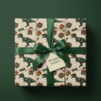 Dinosaur wrapping paper for kids' birthdays, with an emerald ribbon and Wrapped Studios tag.