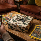 Dinosaur themed birthday wrapping paper with gifts and an "open carefully" tag tied with black string.