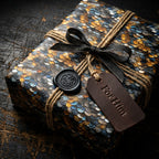 Luxury gift wrap with gold and blue iridescent scale pattern, black ribbon, twine, and "For Him" tag.