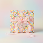 Colorful Easter wrapping paper on a square gift box, tied with sheer pink ribbon and floral tag.