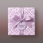 Square gift wrapped in lavender polka dot wrapping paper with satin ribbon bow.
