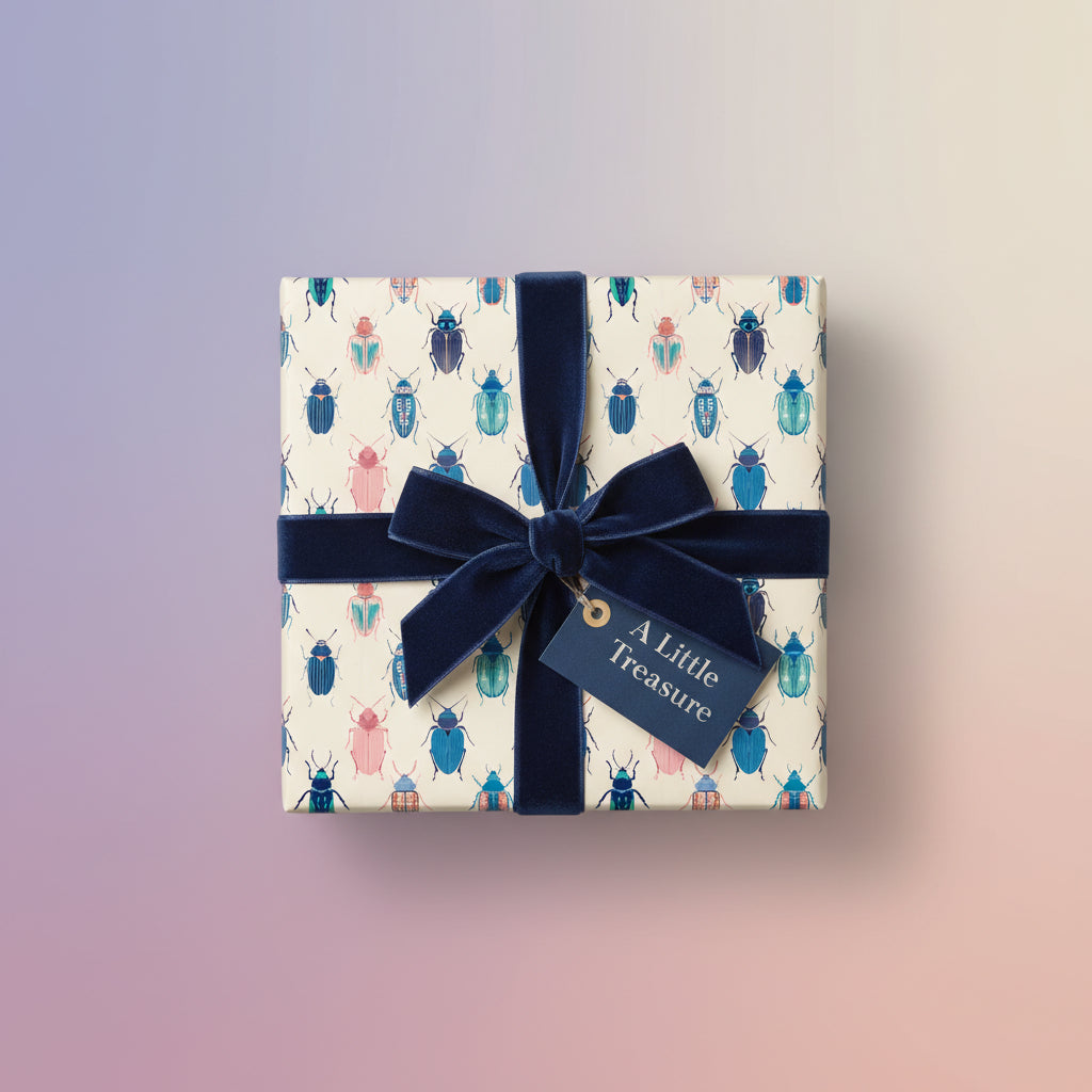 Square gift box wrapped in beetle-patterned wrapping paper with a navy velvet ribbon and "A Little Treasure" gift tag.
